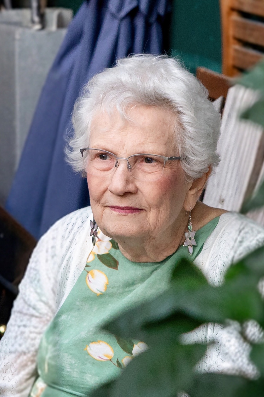 Priscilla Elaine Ferrell, seated outdoors among garden greenery, wearing a green floral dress and white cardigan.