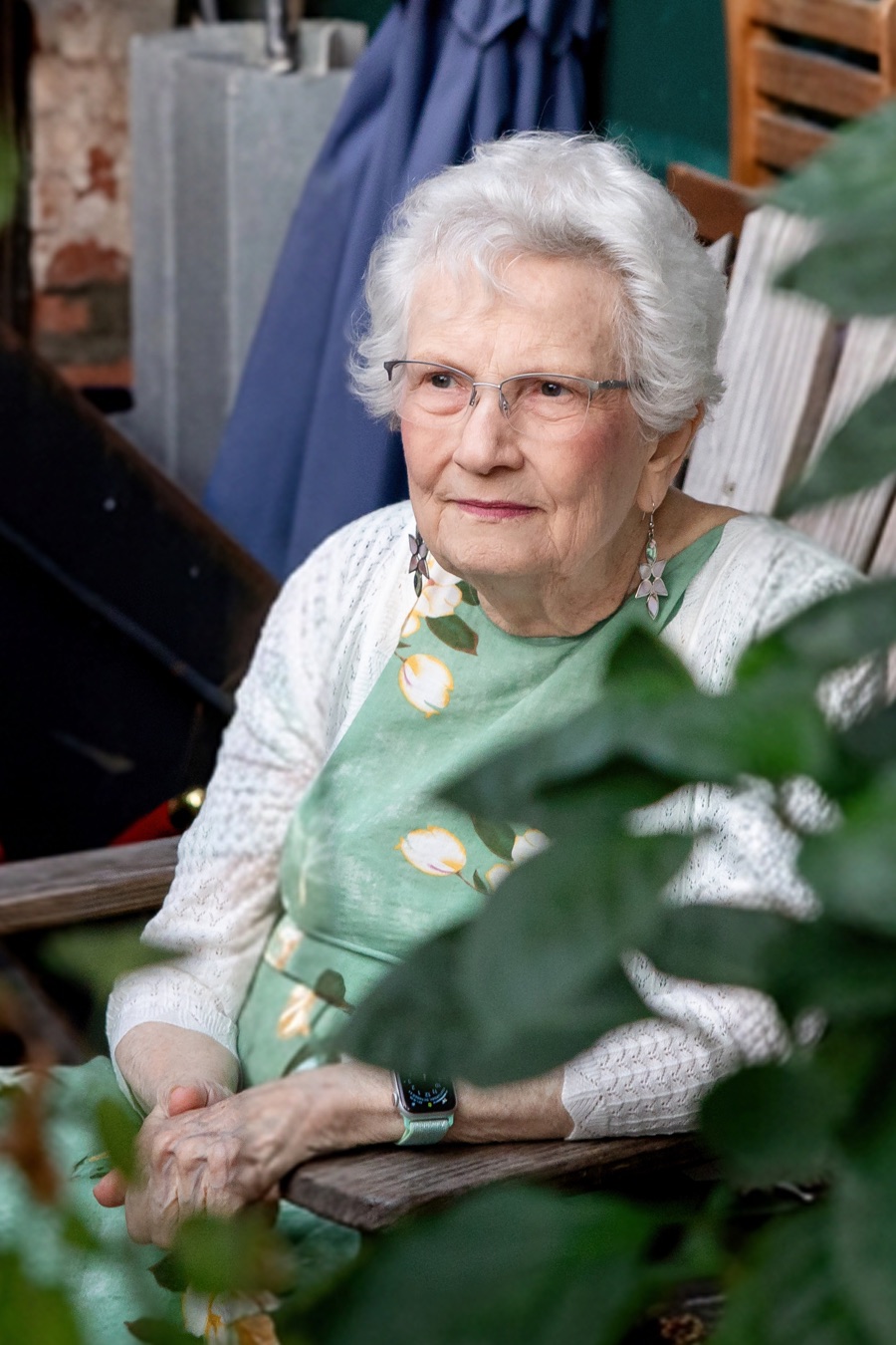 Priscilla Elaine Ferrell, seated outdoors among garden greenery, wearing a green floral dress and white cardigan.